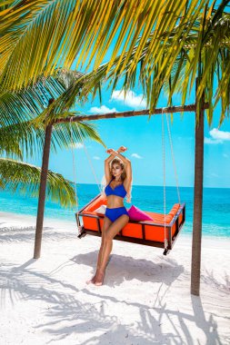 Maldivler tropikal kumsalında seksi bronzlaşmış kadın bikini modeli. Cennette salıncakta sallanan mayolu çekici kız. Mükemmel vücut bikini modeli, uzun sarı saç ve muhteşem Maldivler manzarası. Bikini modeli.