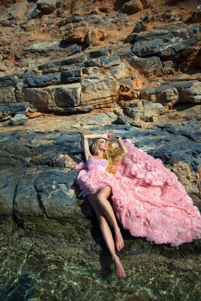 Красива білява жінка сексуальні рожевий бальні сукні стоячи на скелі Санторіні — стокове фото