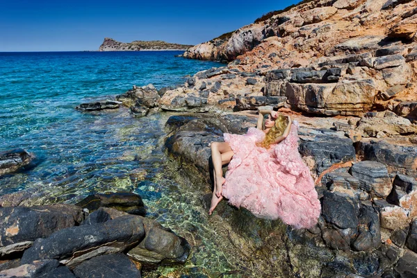 Bella donna bionda sexy abito da sala da ballo rosa in piedi sulle rocce a Santorini — Foto Stock