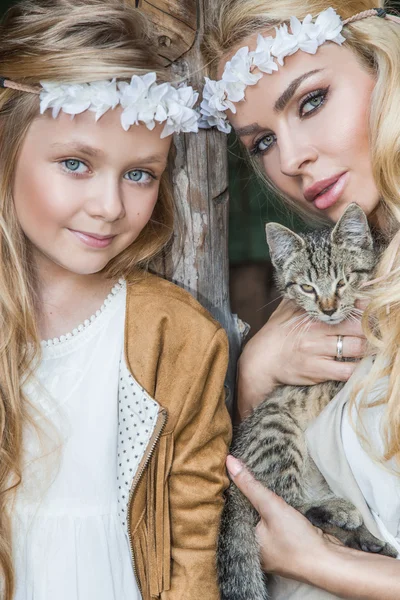 Eine schöne blonde Frau mit einem kleinen Mädchen, das sich im Wilden Westen kuschelt, in weißen Kostümen mit einer Katze an den Händen — Stockfoto