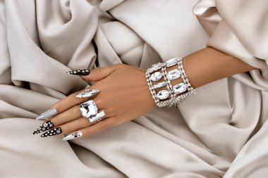 Siyah-beyaz manikür, siyah-beyaz tırnak sanatı ve büyük kristal yüzükler, yumuşak bej kumaş arka planda zarif kadınsı eller.