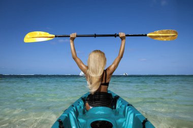 Mauritius 'ta turkuaz okyanus suyunda kano süren bir kadın açık mavi gökyüzü altında damlalar, macera yolculuğu ve tropikal yaşam tarzı kavramı ile kürek çekiyor.