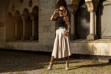 Şık Şık Şık Giyimli Şık Sarışın Kadın Siyah ve Bej Elbiseli, Altın Gün Batımında Klasik Mimarinin yanında duran