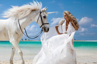 Beyaz elbisesi ve kristal tacı olan zarif bir kadın Mauritius 'da tropik bir plajda görkemli beyaz bir atla birlikte egzotik bir cennette duruyor.