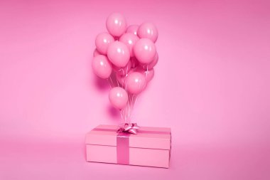 Katı pembe bir arka planda izole edilmiş bir fiyonka bağlı pembe bir balon kümesi olan zarif pembe bir hediye kutusu. Doğum günü partisi sürprizi ya da kutlama için şenlikli bir konsept. Minimalist ve tek renkli estetik..