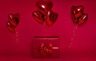 Kırmızı arka planda izole edilmiş bir fiyonka bağlı kırmızı bir balon kümesi olan zarif kırmızı hediye kutusu. Doğum günü, parti, sürpriz veya kutlama için bayram ve sevgililer günü konsepti.