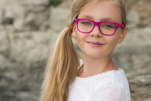 Joven hermosa modelo larga pelo rubio rizado sonriendo en gafas de color rosa y un vestido elegante en la piscina con barandilla y rocas y el mar en España, Grecia, Santorini — Foto de Stock