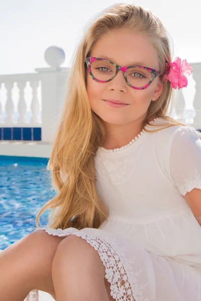 Ung vacker flicka modell långt lockigt blont hår leende i rosa glas och en chic klänning vid poolen med räcke och klippor och havet i Spanien, Grekland, Santorini — Stockfoto