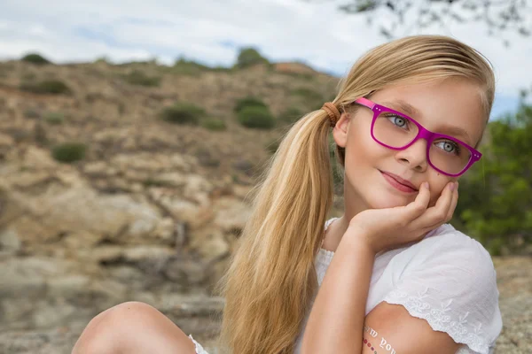 Young beautiful girl model long curly blond hair smiling in pink glasses and a chic dress at the pool with railing and rocks and the sea in Spain, Greece, Santorini — Stock Photo, Image