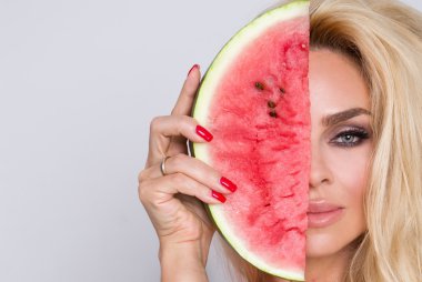 Güzel genç seksi kadın kız sarışın kıvırcık saç uzun sevinçle karpuz ısırıkları ve renkli mayo güzel gülümsüyor vardır mavi gözlü bir beyaz gri arka plan üzerinde