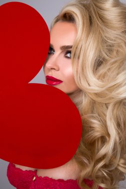 Güzel sarışın seksi kadın modeli kız aşık onun yüz ve kırmızı dudaklar ve kırmızı Erotik çamaşır uzun bacakları kırmızı büyük bir kalbi olan Sevgililer günü