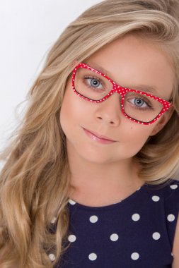 Portrait of a lovely little girl daughter in long blond hair and violet, blue dress with white dots and red glasses with white dots looks at the camera, photo on the white background amazing eyes