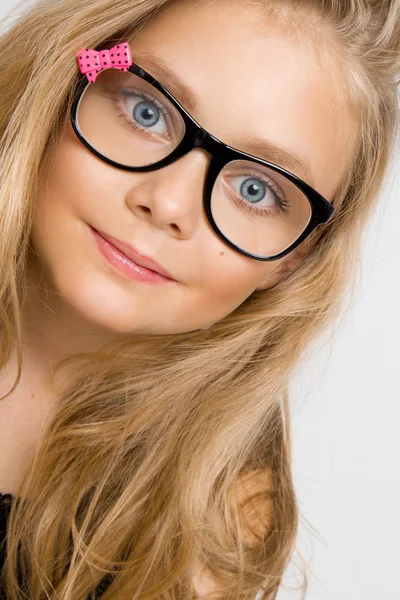 Portrait of a lovely little girl daughter in long blond hair and black glasses with pink bow which looks at the camera, photo on the white background ammazing eyes — Stock Photo, Image