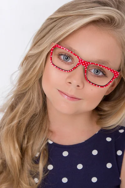 Portrait of a lovely little girl daughter in long blond hair and violet, blue dress with white dots and red glasses with white dots looks at the camera, photo on the white background amazing eyes — Φωτογραφία Αρχείου
