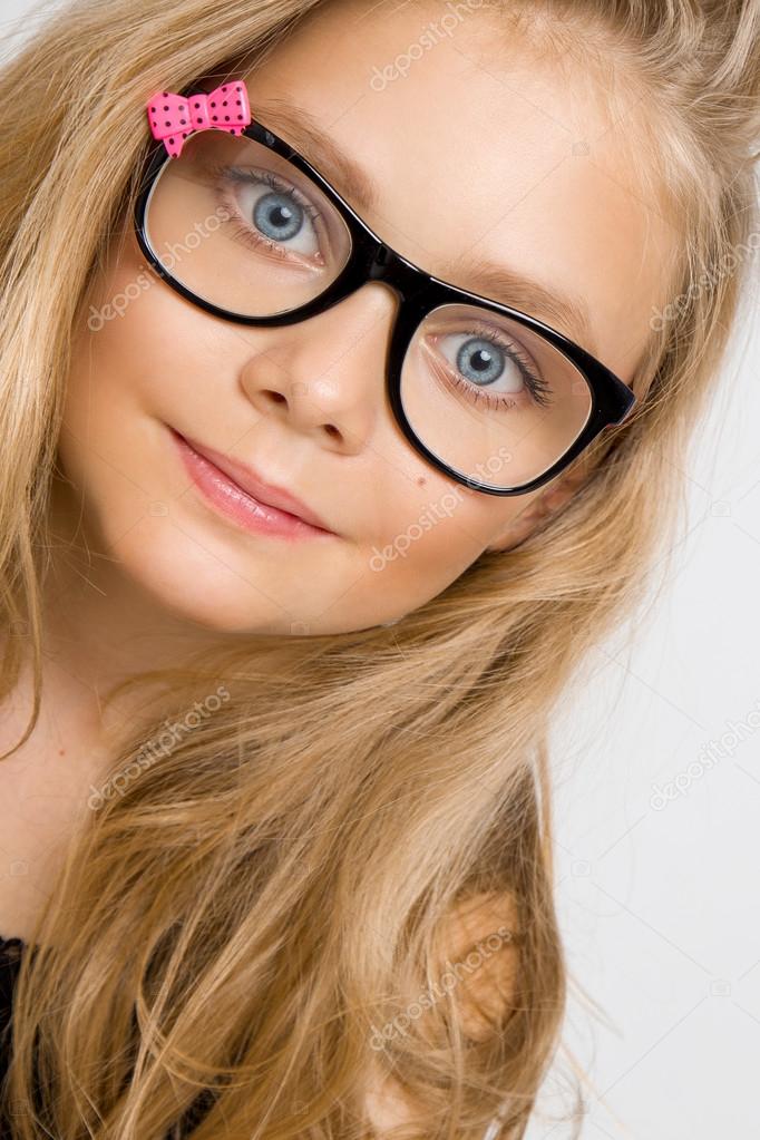 Portrait of a lovely little girl daughter in long blond hair and black glasses with pink bow which looks at the camera, photo on the white background ammazing eyes