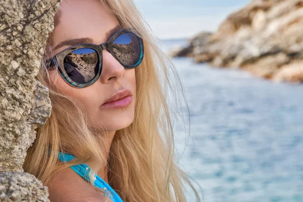 O cabelo loiro muito bonito sexy jovem mulher modelo em óculos de sol em ouro tatoo está de pé no maiô azul erótico e cristais lingerie nas rochas — Fotografia de Stock