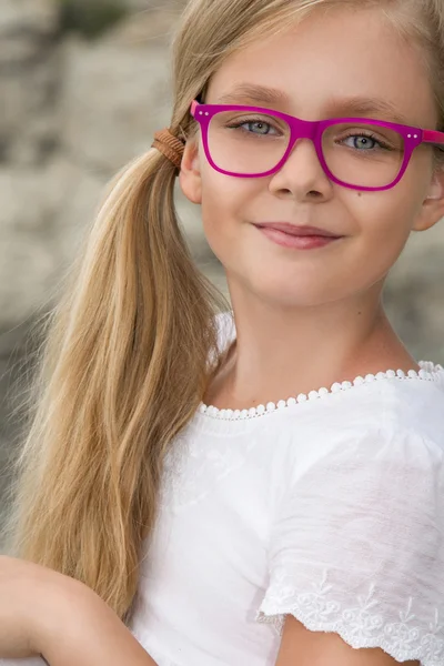 Young beautiful child girl model long curly blond hair smiling in pink glasses and a chic elegant dress at the rocks and the sea in Spain, Greece, Santorini — Stock fotografie