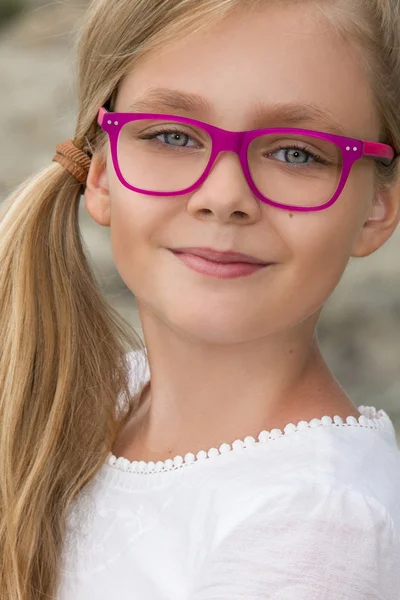 Joven hermosa niña modelo largo pelo rubio rizado sonriendo en gafas de color rosa y un elegante vestido elegante en las rocas y el mar en España, Grecia, Santorini — Foto de Stock