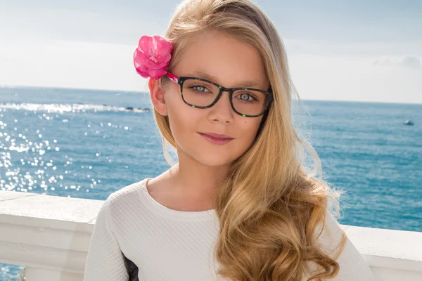 Young beautiful child girl model long curly blond hair smiling in pink glasses and a chic elegant long blacj and white dress at the pool and the sea in Spain, Greece, Santorini — ストック写真