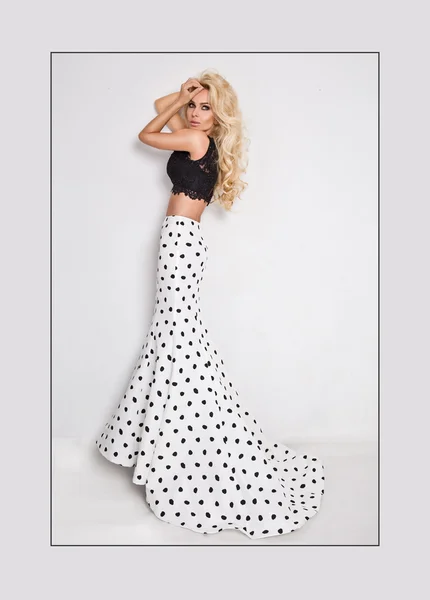 Schöne Blondine mit langen lockigen Haaren junge Frau im weißen Modell schwarzen Ballkleid, eine Polka-Farbe mit einer langen Schleppe auf weißem Hintergrund — Stockfoto