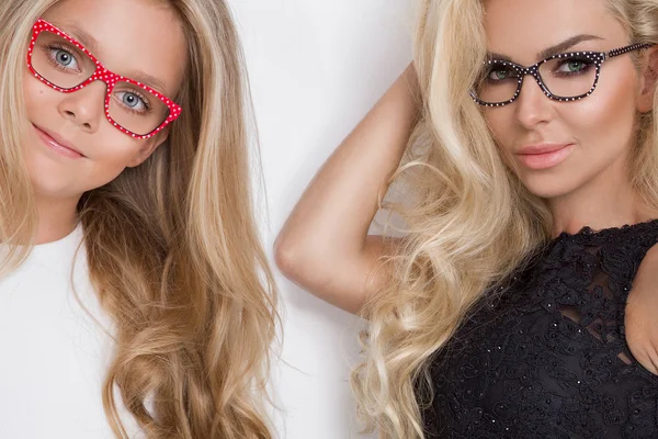 The beautiful blond hair woman my mother very with green eyes lace blouse and a polka dot short skirt in a sensual hairstyle with black glasses with daughter girl in a white dress in pink glasses on a white background — Stock Photo, Image