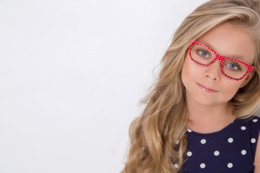 Kameranın resmi beyaz arka plan şaşırtıcı gözleri için bir güzel küçük kız kızı uzun sarı saçlı ve beyaz elbise ve beyaz noktalı kırmızı gözlük portresi bakar