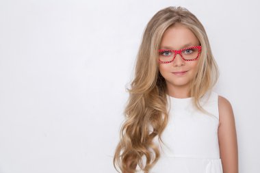 Kameranın resmi beyaz arka plan şaşırtıcı gözleri için bir güzel küçük kız kızı uzun sarı saçlı ve beyaz elbise ve beyaz noktalı kırmızı gözlük portresi bakar