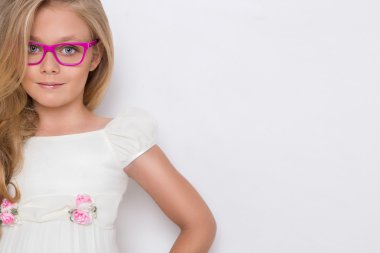 Kameranın resmi beyaz arka plan şaşırtıcı gözleri için bir güzel küçük kız kızı uzun sarı saçlı ve beyaz elbise ve beyaz noktalı kırmızı gözlük portresi bakar