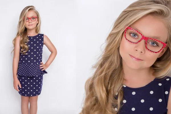 Portrait of a lovely little girl daughter in long blond hair and violet, blue dress with white dots and red glasses with white dots looks at the camera, photo on the white background amazing eyes — Stockfoto