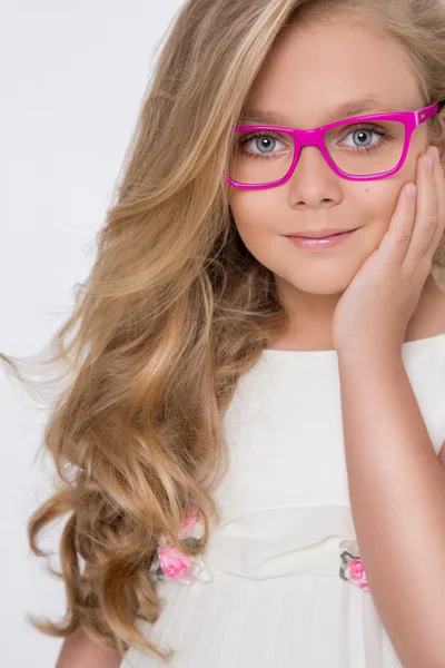 Retrato de una encantadora hija niña en pelo largo y rubio y vestido blanco y gafas rojas con puntos blancos mira a la cámara, foto sobre el fondo blanco ojos increíbles —  Fotos de Stock