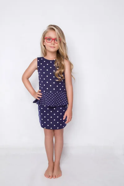 Portrait of a lovely little girl daughter in long blond hair and violet, blue dress with white dots and red glasses with white dots looks at the camera, photo on the white background amazing eyes — Stock fotografie