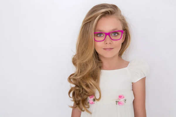 Portrait of a lovely little girl daughter in long blond hair and white dress and red glasses with white dots looks at the camera, photo on the white background amazing eyes — Stock Photo, Image