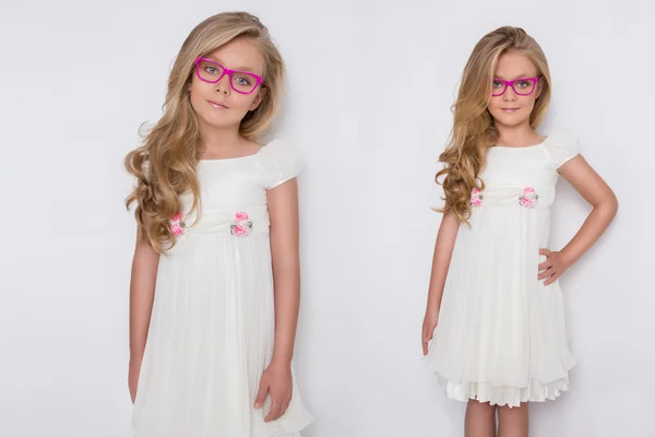 Retrato de una encantadora hija niña en pelo largo y rubio y vestido blanco y gafas rojas con puntos blancos mira a la cámara, foto sobre el fondo blanco ojos increíbles — Foto de Stock