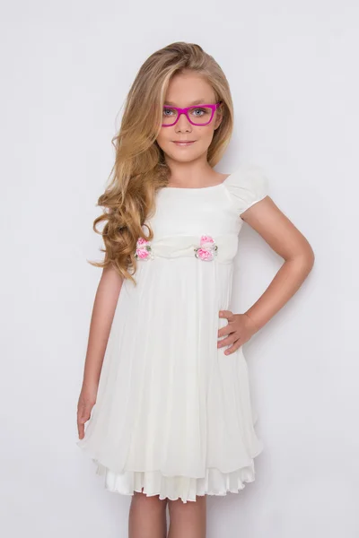 Porträtt av en härlig liten flicka dotter i långa blonda hår och vit klänning och röda glas med vita prickar ser på kameran, foto på vit bakgrund fantastiska ögonen — Stockfoto