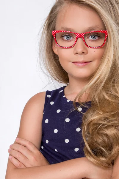 Retrato de uma linda filha menina no cabelo loiro longo e violeta, vestido azul com pontos brancos e óculos vermelhos com pontos brancos olha para a câmera, foto no fundo branco olhos surpreendentes — Fotografia de Stock
