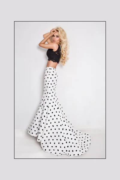 Beautiful blond with long curly hair young woman in the white model black ball gown, a polka color with a long train on a white background Stock Photo