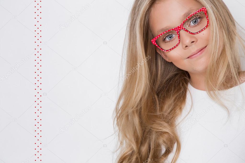 Portrait of a lovely little girl daughter in long blond hair and white dress and red glasses with white dots looks at the camera, photo on the white background amazing eyes