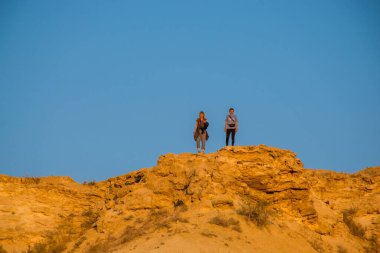 Mavi gökyüzü arka planında, çölde bir çift yürüyüşçü.