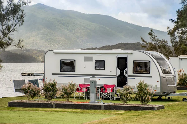 Karavan karavanı, ufukta dağları olan huzurlu bir göl üzerindeki karavan parkında kamp yapıyor. Kamp gezisi aile seyahati