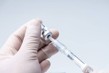 Doktor elinde grip olan beyaz bir eldiven takıyor, kovid 19 sıvı aşı şişesi ve şırınga enjeksiyona hazırlanıyor. Covid-19 virüs kavramına karşı aşı.