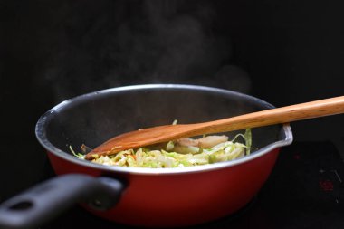 İndüksiyon fırınıyla teflon pan ısı kaynağında karışık sebzeleri karıştır.