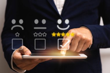 İşadamı, işaretli kutuda elinde tablet bulunan 5 yıldızlı gülümseme simgesini seçin ve iyi notu gözden geçirmek için ekranda parmak dokunuşunu kullanın. En iyi deneyim ve müşteri hizmetleri geri bildirim kavramı.