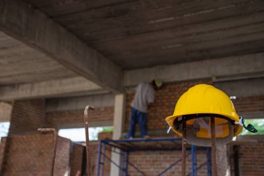 Sarı kasklı inşaat işçisi dış duvarları inşa etmek için betona tuğla koyuyor..