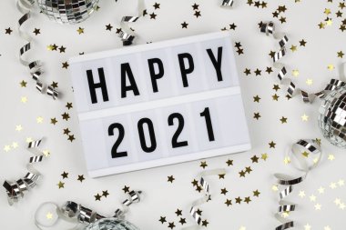 lightbox with words happy 2021, disco ball, ribbon and holiday confetti on white background. top view. Happy New Year 2021 concept. 