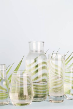 Palmiye yaprağı bardaklarda ve mavi arka planda şişelerde suda bozulur. Ev dekorasyonu, çevre dostu, saf su, bahçe kavramı.