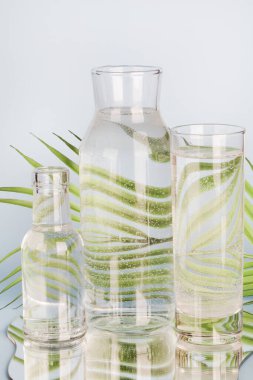 Palmiye yaprağı, cam içinde su ve mavi arka planda ayna olan şişeler içinde bozulur. Ev dekorasyonu, çevre dostu, saf su, bahçe konsepti..