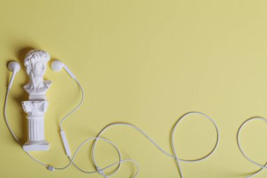 Sarı arka planda küçük heykeli olan beyaz kulaklıklar. Üst görünüm düz kopya alanı