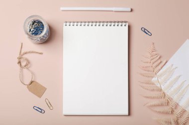 Ofis masası çalışma alanı, defter, kalem, ataç, boş kağıt etiketi ve bej arka planda eğreltiotu. Düzlük, iş, iş, modelleme konsepti. Boşluğu kopyala.