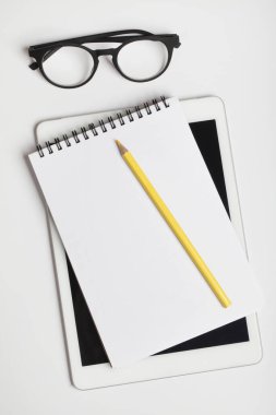 Ofis masası, dijital tabletli çalışma alanı, defter, sarı kalem ve gözlük.. 