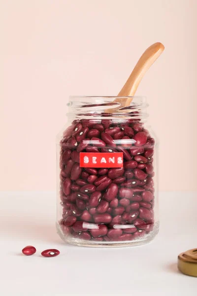 Червоні боби в скляній банці з дерев'яною ложкою на бежевому та білому тлі. концепція способу життя охорони здоров'я . — стокове фото